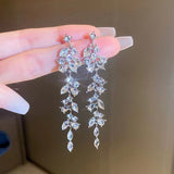 Elegant silver earrings with clear stones held by a hand against a neutral background